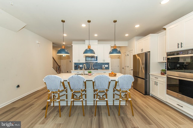 kitchen with appliances with stainless steel finishes, hanging light fixtures, white cabinetry, and decorative backsplash