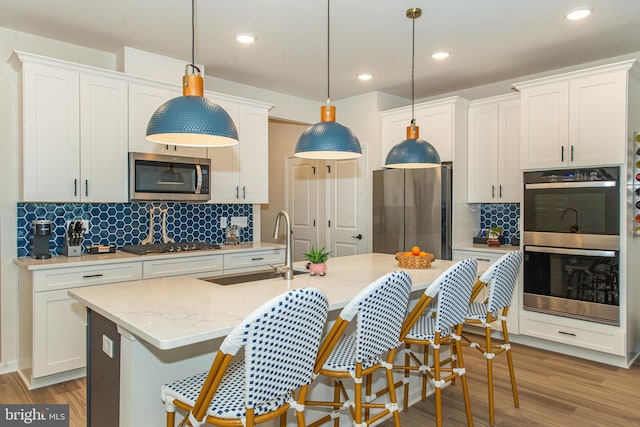 kitchen featuring stainless steel appliances, sink, a kitchen island with sink, and hanging light fixtures