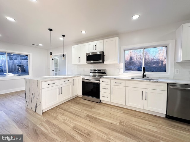 kitchen featuring sink, appliances with stainless steel finishes, white cabinetry, hanging light fixtures, and kitchen peninsula