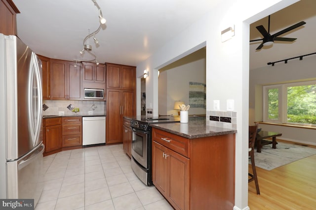 kitchen featuring appliances with stainless steel finishes, tasteful backsplash, dark stone counters, ceiling fan, and light tile patterned flooring