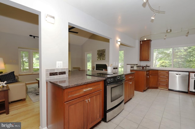 kitchen with kitchen peninsula, stainless steel appliances, dark stone countertops, lofted ceiling, and light tile patterned flooring