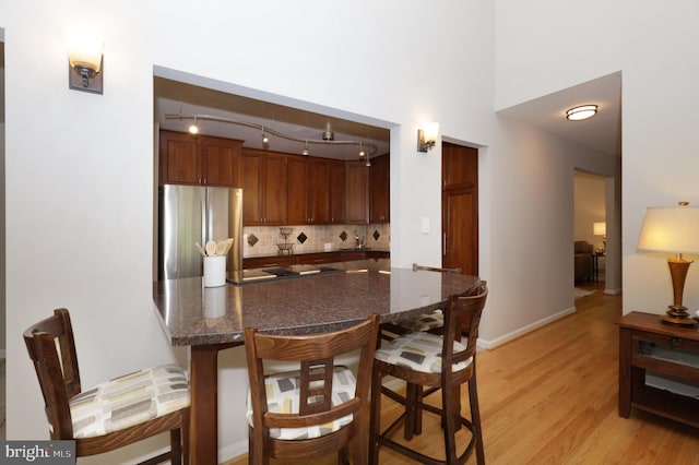 kitchen featuring kitchen peninsula, light wood-type flooring, backsplash, and stainless steel refrigerator