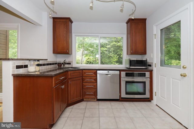 kitchen with sink, dark stone countertops, light tile patterned floors, appliances with stainless steel finishes, and tasteful backsplash