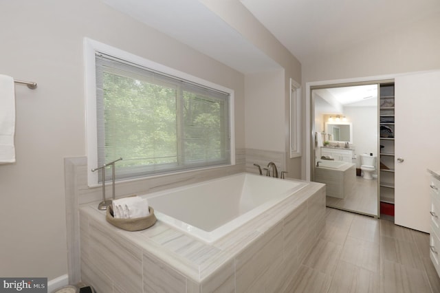 bathroom with vanity, a relaxing tiled tub, tile patterned floors, and lofted ceiling