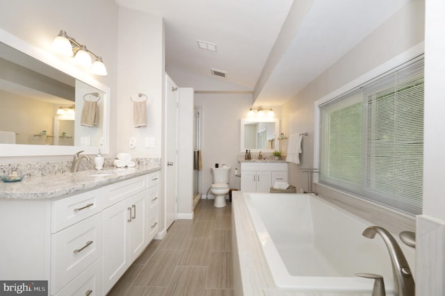 bathroom featuring tiled tub, vanity, lofted ceiling, and toilet