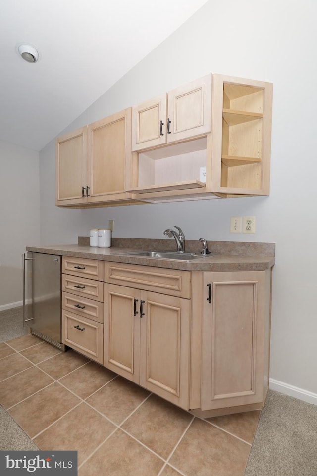 kitchen with light brown cabinetry, vaulted ceiling, sink, light tile patterned floors, and stainless steel refrigerator