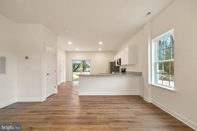 kitchen with dark wood-type flooring, stainless steel appliances, light stone counters, kitchen peninsula, and white cabinets