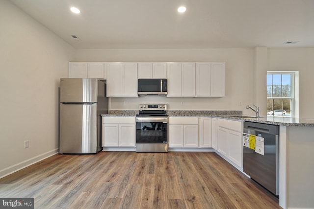 kitchen featuring white cabinetry, light stone counters, hardwood / wood-style flooring, and appliances with stainless steel finishes