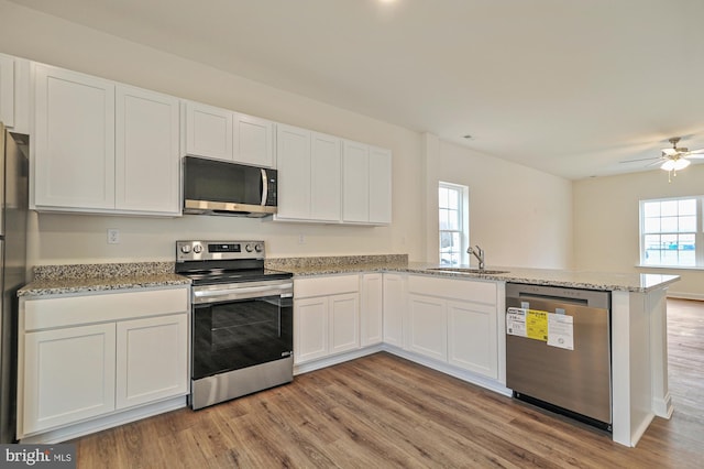 kitchen featuring sink, light hardwood / wood-style flooring, kitchen peninsula, white cabinets, and appliances with stainless steel finishes