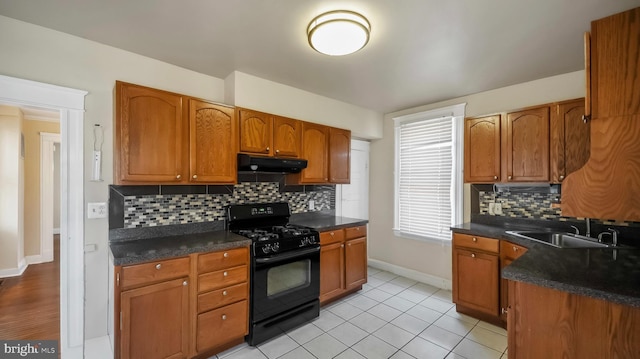 kitchen featuring brown cabinetry, dark countertops, black range with gas stovetop, under cabinet range hood, and a sink