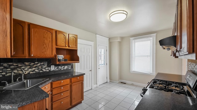 kitchen featuring a sink, range hood, backsplash, brown cabinets, and gas range