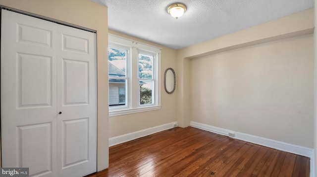 spare room featuring dark wood-style floors, a textured ceiling, and baseboards