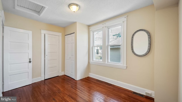 interior space featuring a textured ceiling, visible vents, baseboards, dark wood-style floors, and attic access