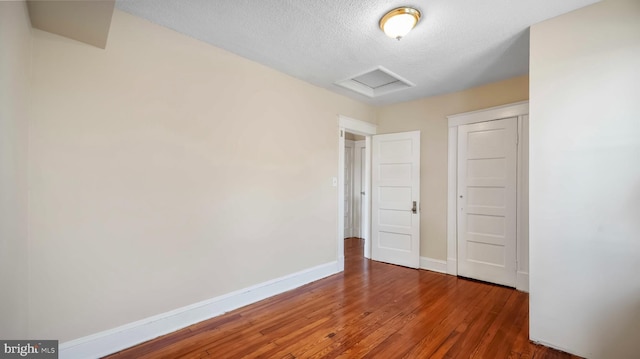 unfurnished bedroom featuring a textured ceiling, wood finished floors, attic access, and baseboards