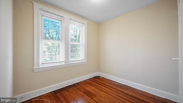 spare room with dark wood-style floors, a textured ceiling, and baseboards