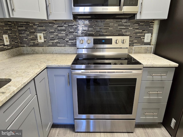 kitchen featuring stainless steel appliances, decorative backsplash, gray cabinetry, and light stone counters