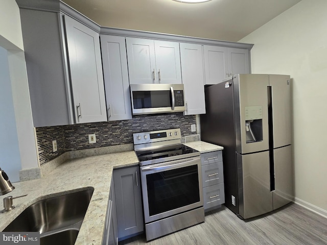 kitchen featuring light stone countertops, stainless steel appliances, tasteful backsplash, gray cabinets, and sink