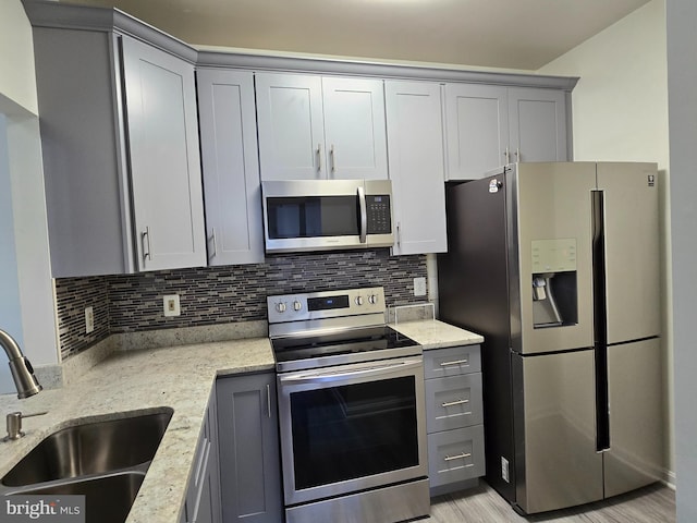 kitchen featuring gray cabinets, stainless steel appliances, light stone countertops, sink, and tasteful backsplash