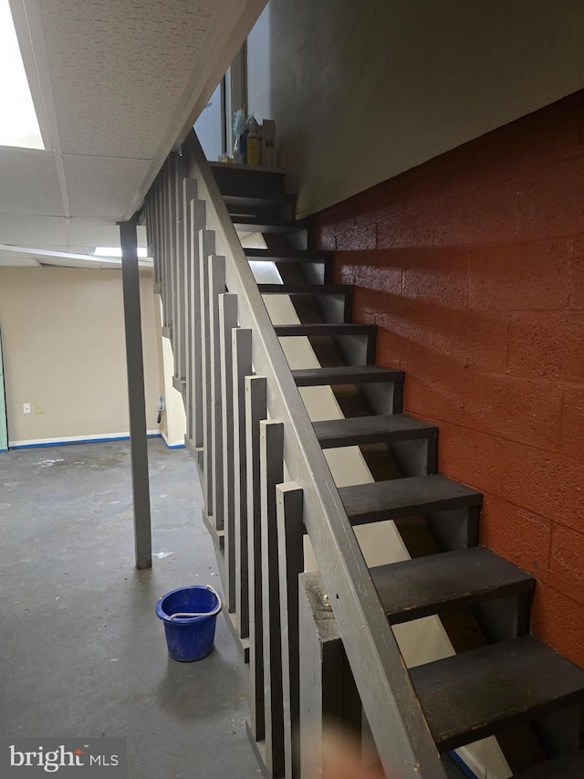 staircase with concrete floors and a paneled ceiling