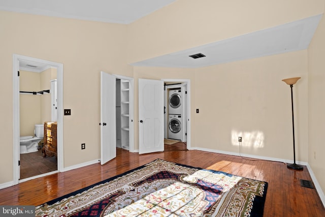 bedroom with a walk in closet, connected bathroom, stacked washer / dryer, and wood-type flooring