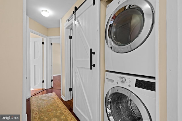 clothes washing area with stacked washer / dryer, a barn door, and dark hardwood / wood-style floors