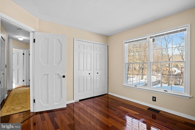 unfurnished bedroom featuring a closet, multiple windows, and dark hardwood / wood-style floors