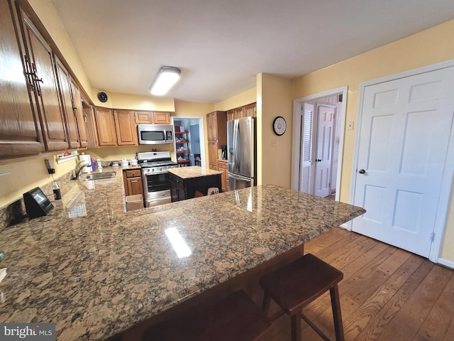 kitchen with dark hardwood / wood-style floors, kitchen peninsula, sink, appliances with stainless steel finishes, and a kitchen breakfast bar