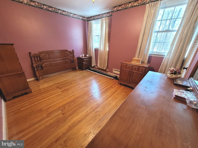 bedroom with baseboard heating, multiple windows, and light hardwood / wood-style flooring