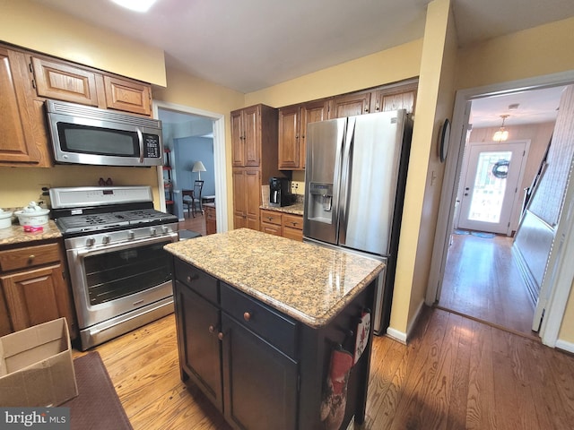 kitchen with light stone countertops, appliances with stainless steel finishes, a center island, and light wood-type flooring