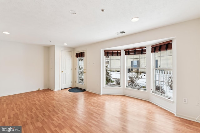 empty room with a textured ceiling and light hardwood / wood-style flooring