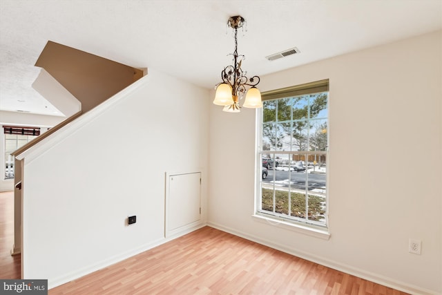 unfurnished dining area with an inviting chandelier and light wood-type flooring