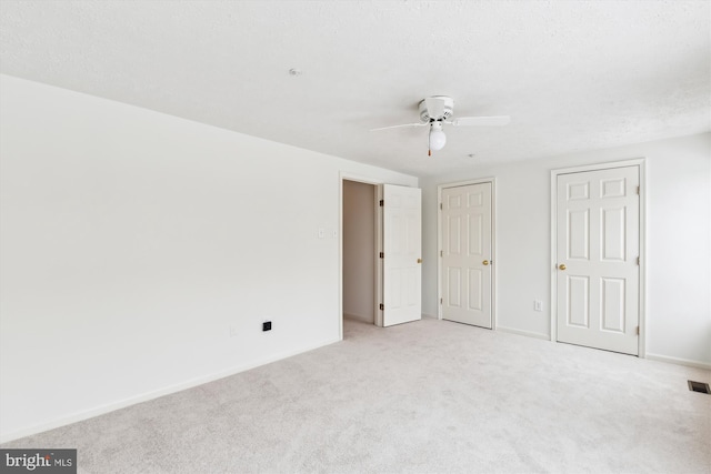 unfurnished bedroom with ceiling fan, two closets, light carpet, and a textured ceiling