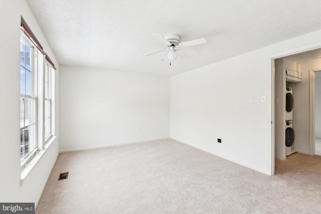 spare room with light colored carpet, ceiling fan, and stacked washer and clothes dryer