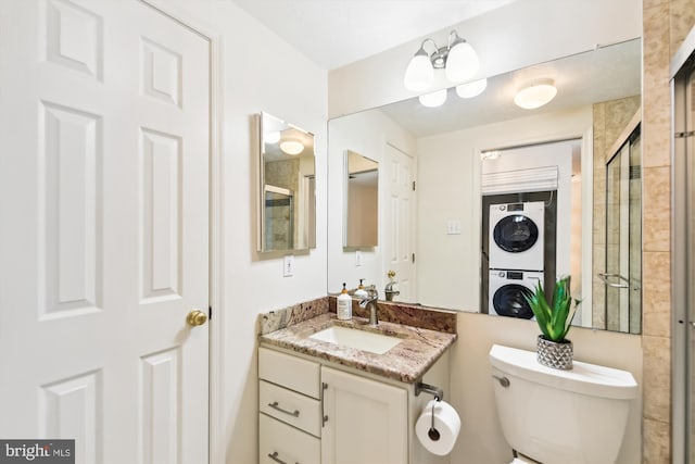 bathroom featuring stacked washer and clothes dryer, a shower with door, vanity, and toilet