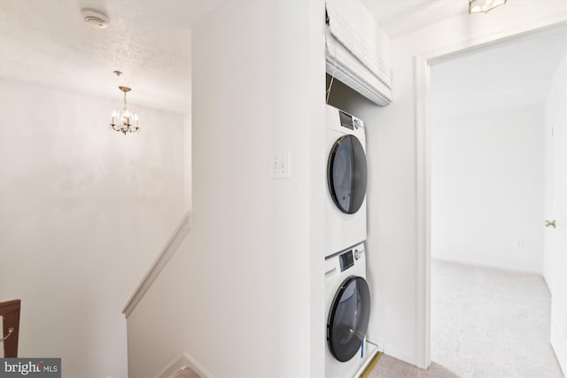 laundry area with a textured ceiling, a notable chandelier, light carpet, and stacked washer / drying machine