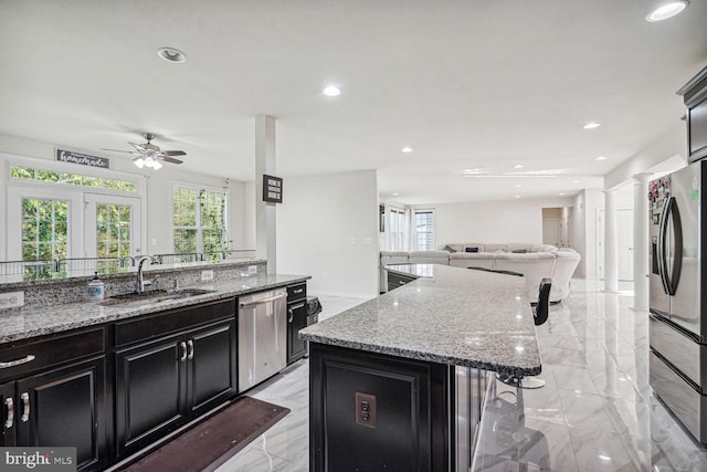 kitchen with appliances with stainless steel finishes, a center island, light stone counters, and sink