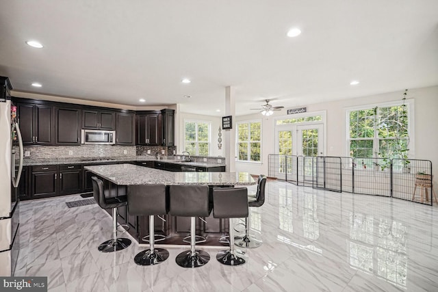 kitchen featuring light stone countertops, a center island, ceiling fan, stainless steel appliances, and backsplash