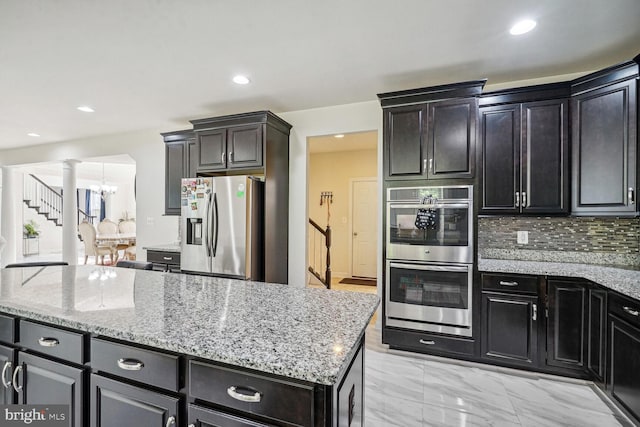 kitchen with backsplash, ornate columns, a notable chandelier, light stone counters, and stainless steel appliances