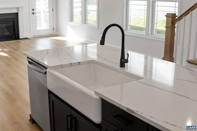 kitchen with a wealth of natural light, light stone counters, sink, and stainless steel dishwasher