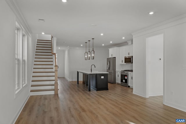 kitchen with hanging light fixtures, a kitchen breakfast bar, a kitchen island with sink, white cabinets, and appliances with stainless steel finishes