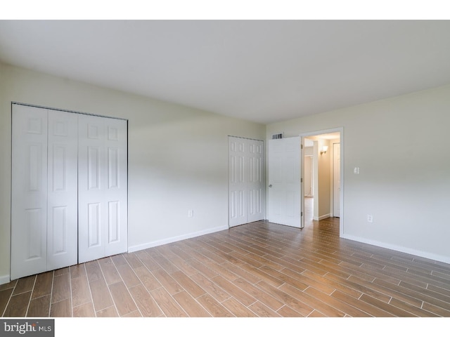 unfurnished bedroom with two closets and hardwood / wood-style floors