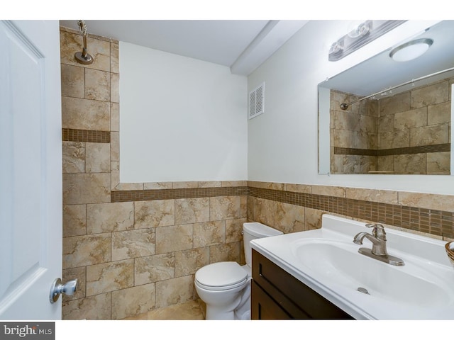 bathroom featuring vanity, toilet, and tile walls