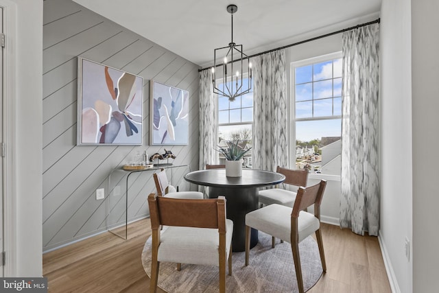 dining area with a chandelier, light hardwood / wood-style flooring, and wood walls