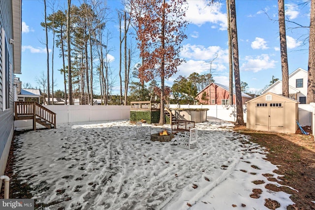 yard covered in snow featuring an outdoor fire pit, a jacuzzi, and a storage shed