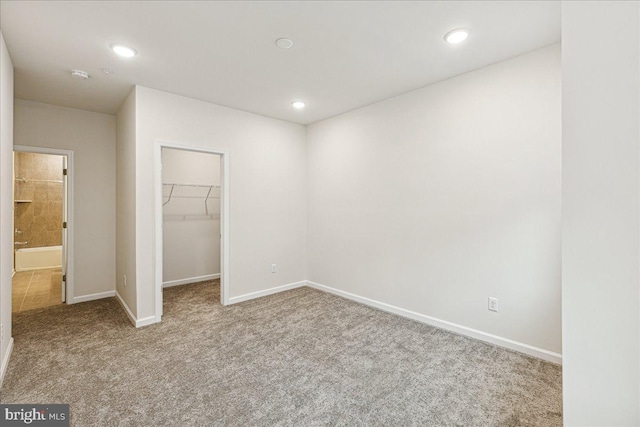 unfurnished bedroom with a walk in closet, a closet, and light colored carpet