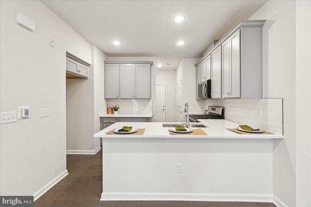 kitchen with kitchen peninsula, appliances with stainless steel finishes, dark hardwood / wood-style flooring, decorative backsplash, and sink