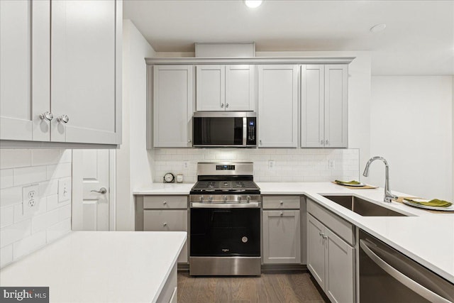 kitchen with sink, decorative backsplash, gray cabinets, dark hardwood / wood-style floors, and appliances with stainless steel finishes