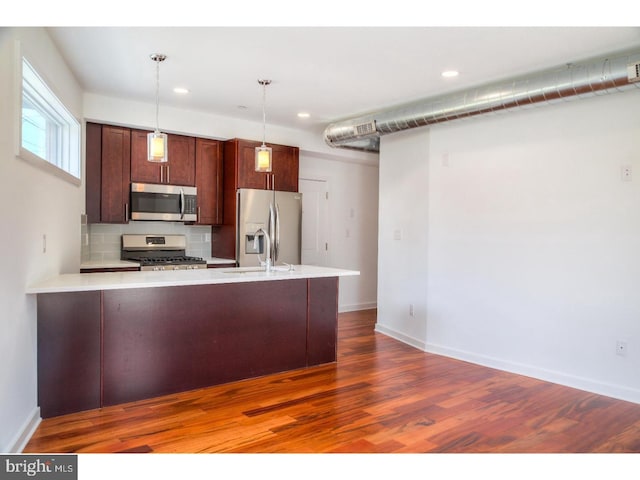 kitchen featuring decorative backsplash, appliances with stainless steel finishes, decorative light fixtures, dark hardwood / wood-style flooring, and kitchen peninsula