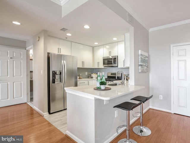 kitchen featuring kitchen peninsula, stainless steel appliances, sink, white cabinets, and a breakfast bar area