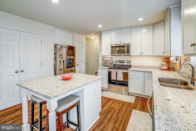 kitchen with light stone countertops, white cabinets, stainless steel appliances, sink, and a breakfast bar